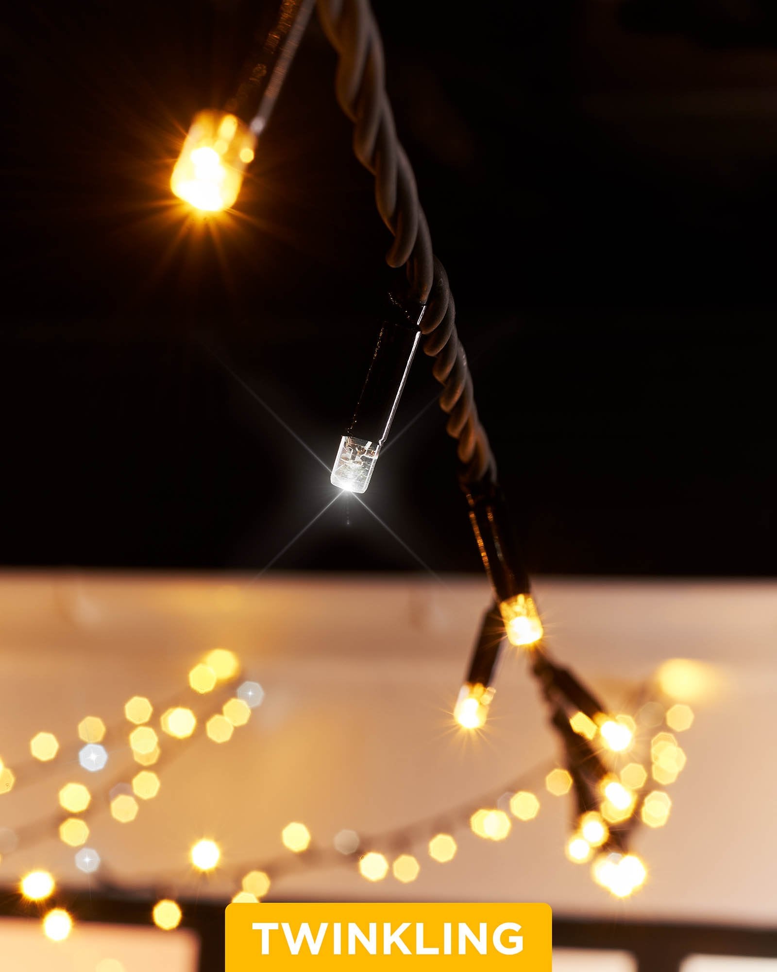 Close-up of connectable twinkle string lights with warm white and white LEDs, showcasing the twinkle effect. The image is taken during the evening with a blurred background.