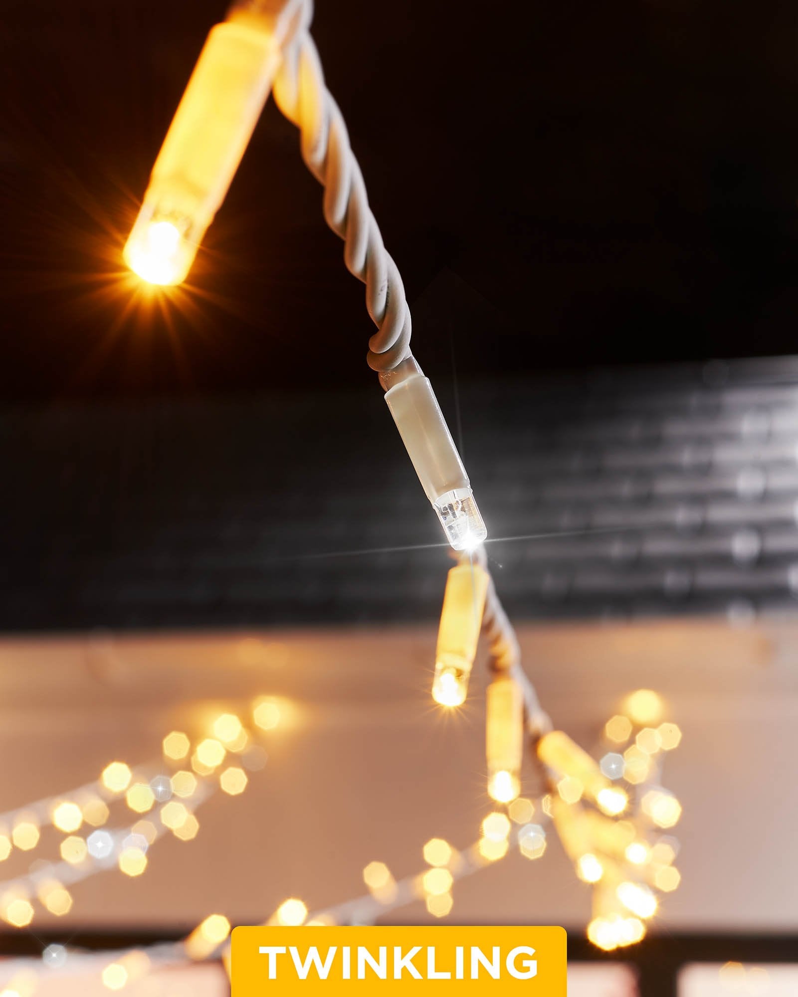 Close-up of connectable twinkle string lights with warm white and white LEDs, showcasing the twinkle effect. The image is taken during the evening with a blurred background.