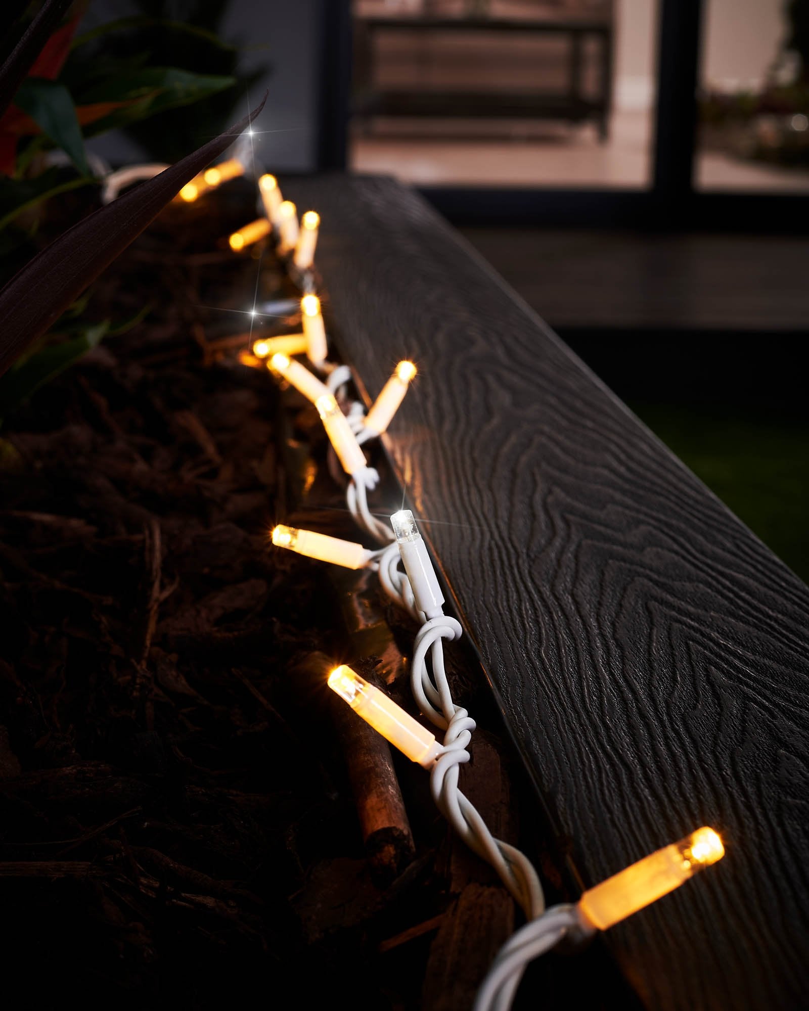 Close-up of connectable twinkle string lights with warm white and white LEDs, showcasing the twinkle effect. The image is taken during the evening with a blurred background.