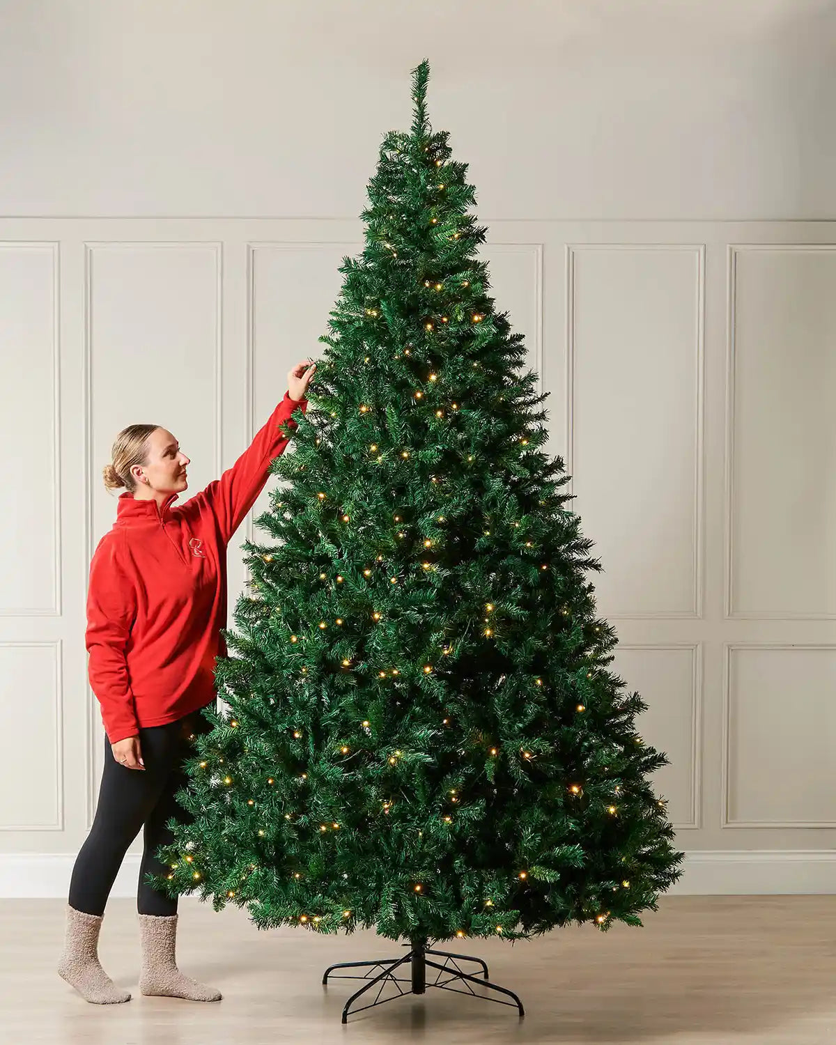 Lady in a red jumper and beige socks next to a Christmas tree against a cream panel wall