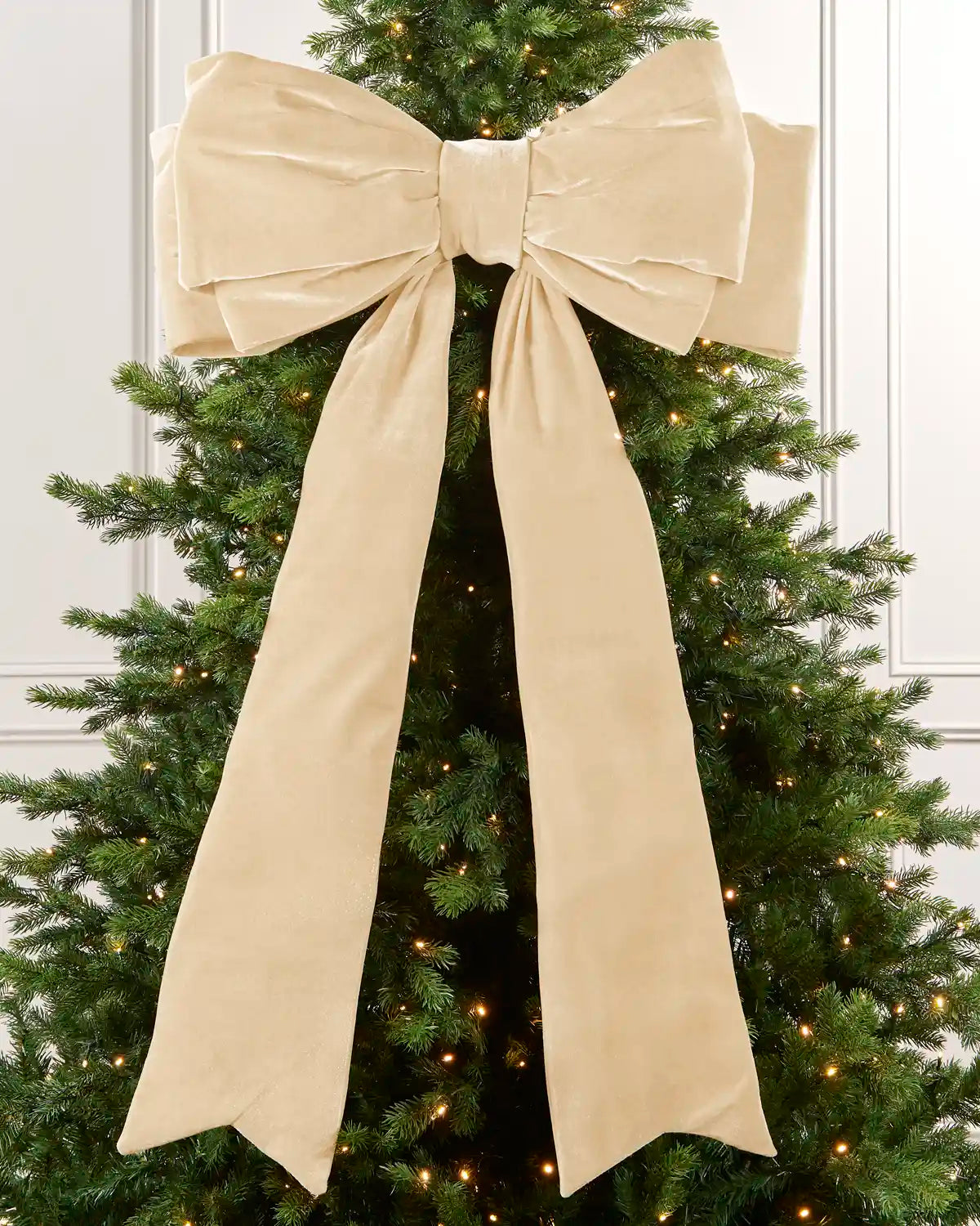 Large 140 cm latte velvet Christmas bow displayed on a lit Christmas tree with long hanging tails.
