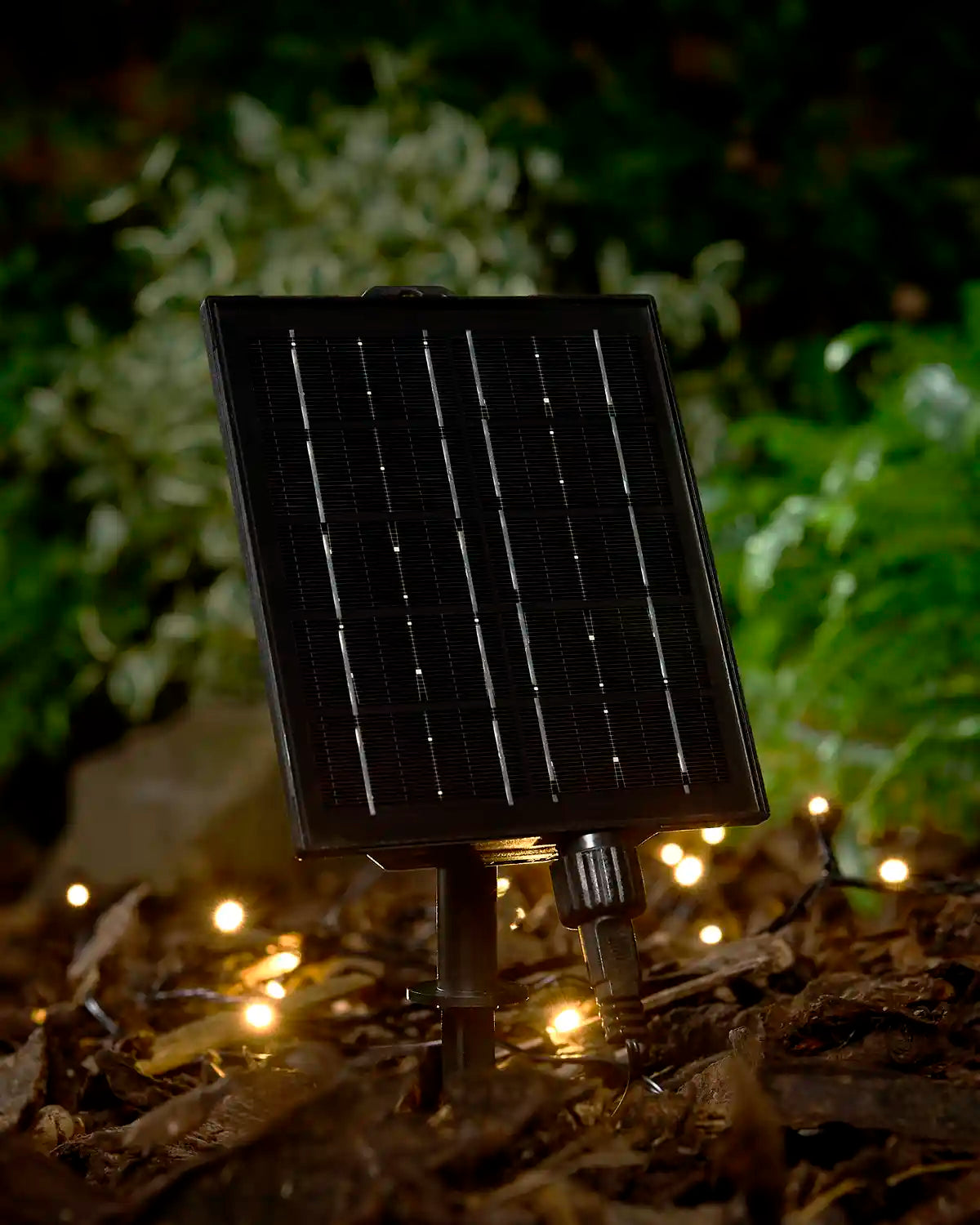 Large black solar panel in the ground attached to warm white LEDs with a blurry garden background