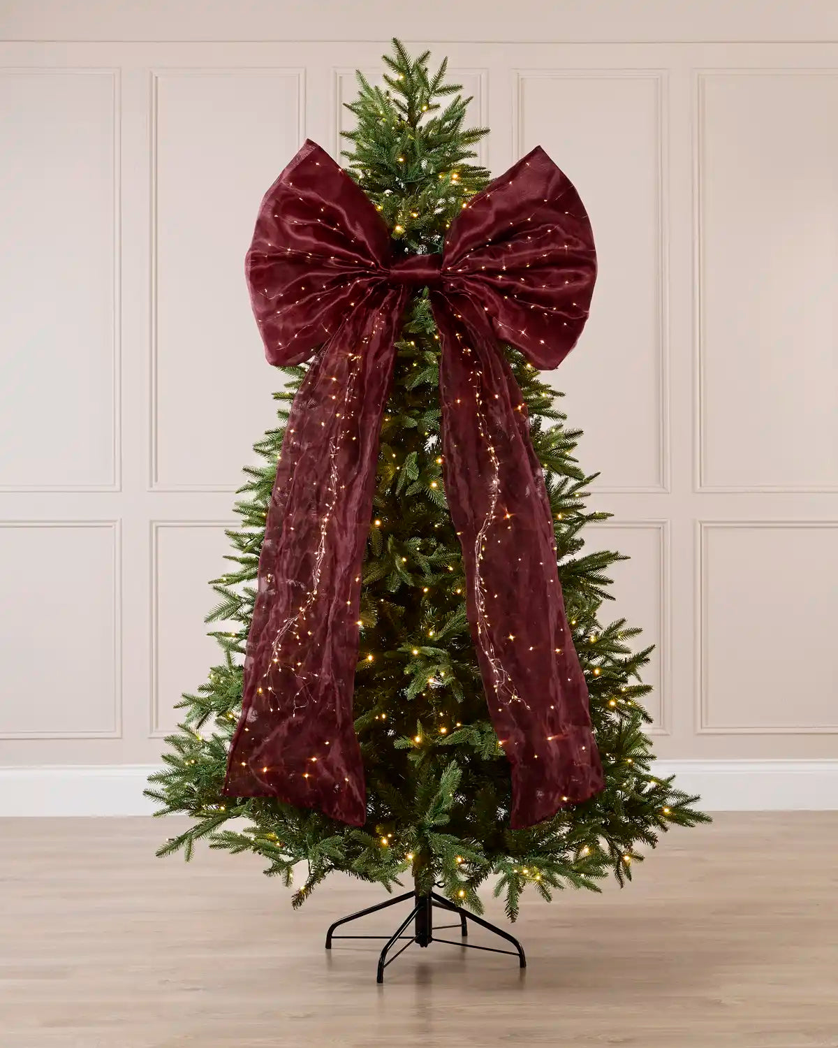 Large burgundy Christmas bow with warm white lights displayed on a decorated Christmas tree.