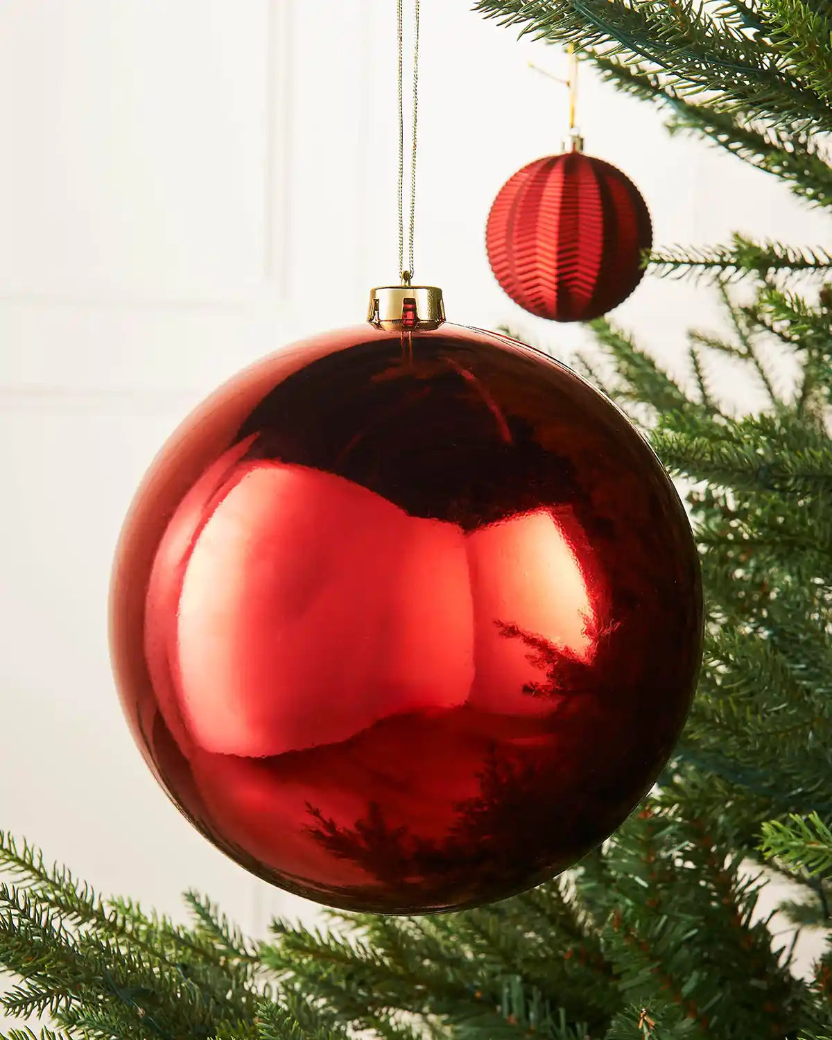 Large oversized Red gloss bauble on the middle of a Christmas tree branch accompanied by a smaller red textured bauble