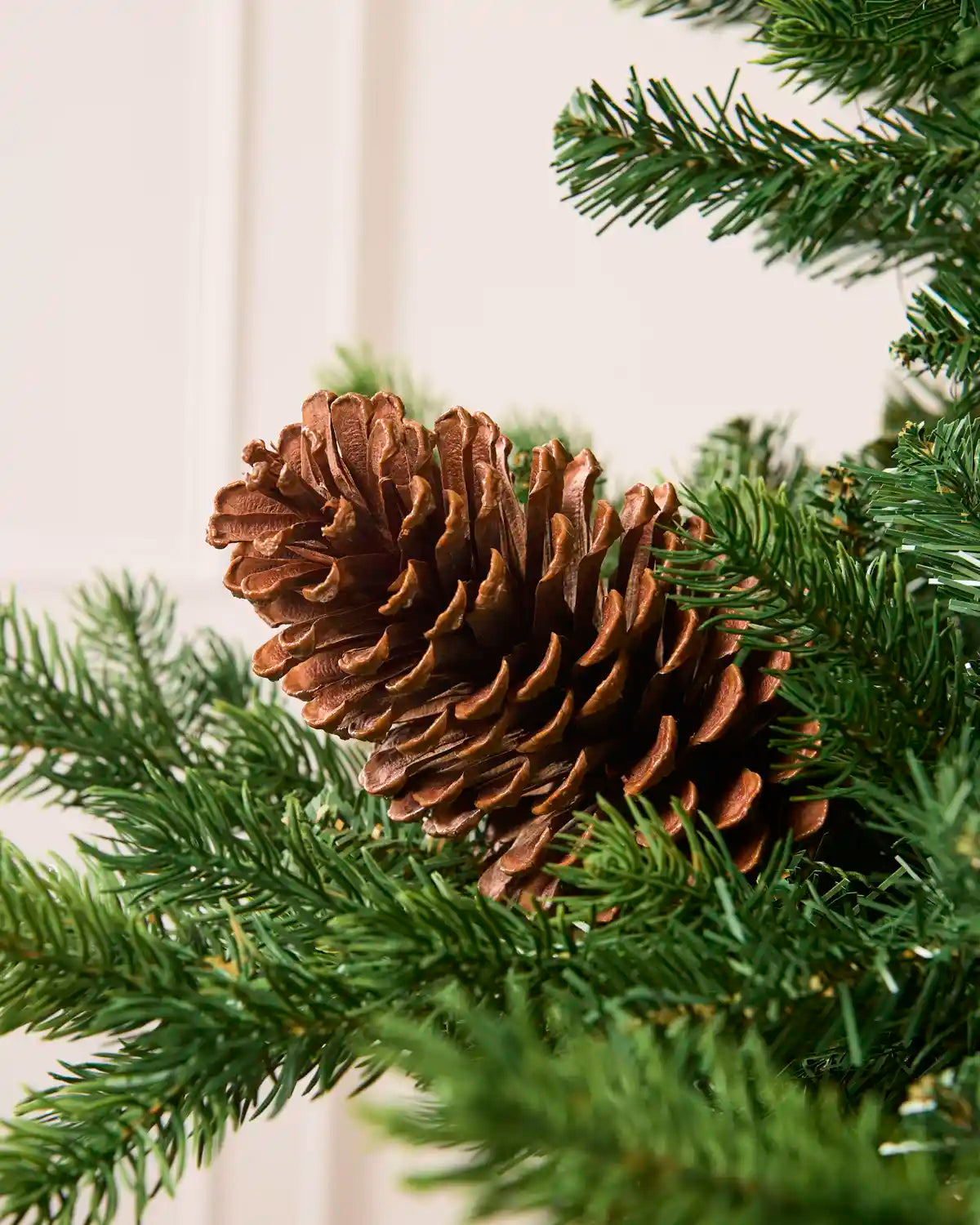 Large pinecone placed on a Christmas tree branch with a blurred cream background