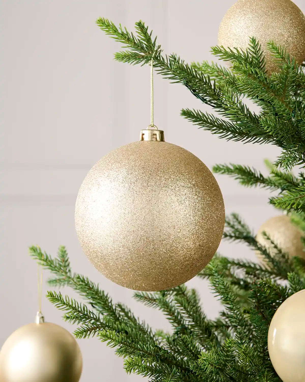 Latte 15 cm oversized glitter shatterproof bauble displayed on a Christmas tree with coordinating latte baubles.
