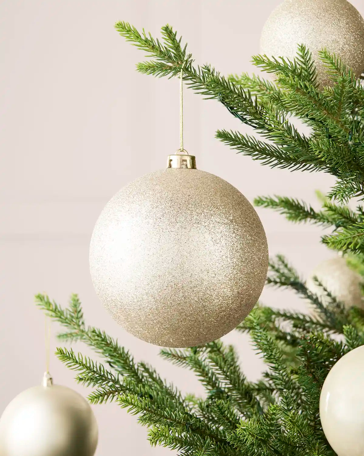 Latte 15 cm oversized glitter shatterproof bauble displayed on a Christmas tree with coordinating latte baubles.
