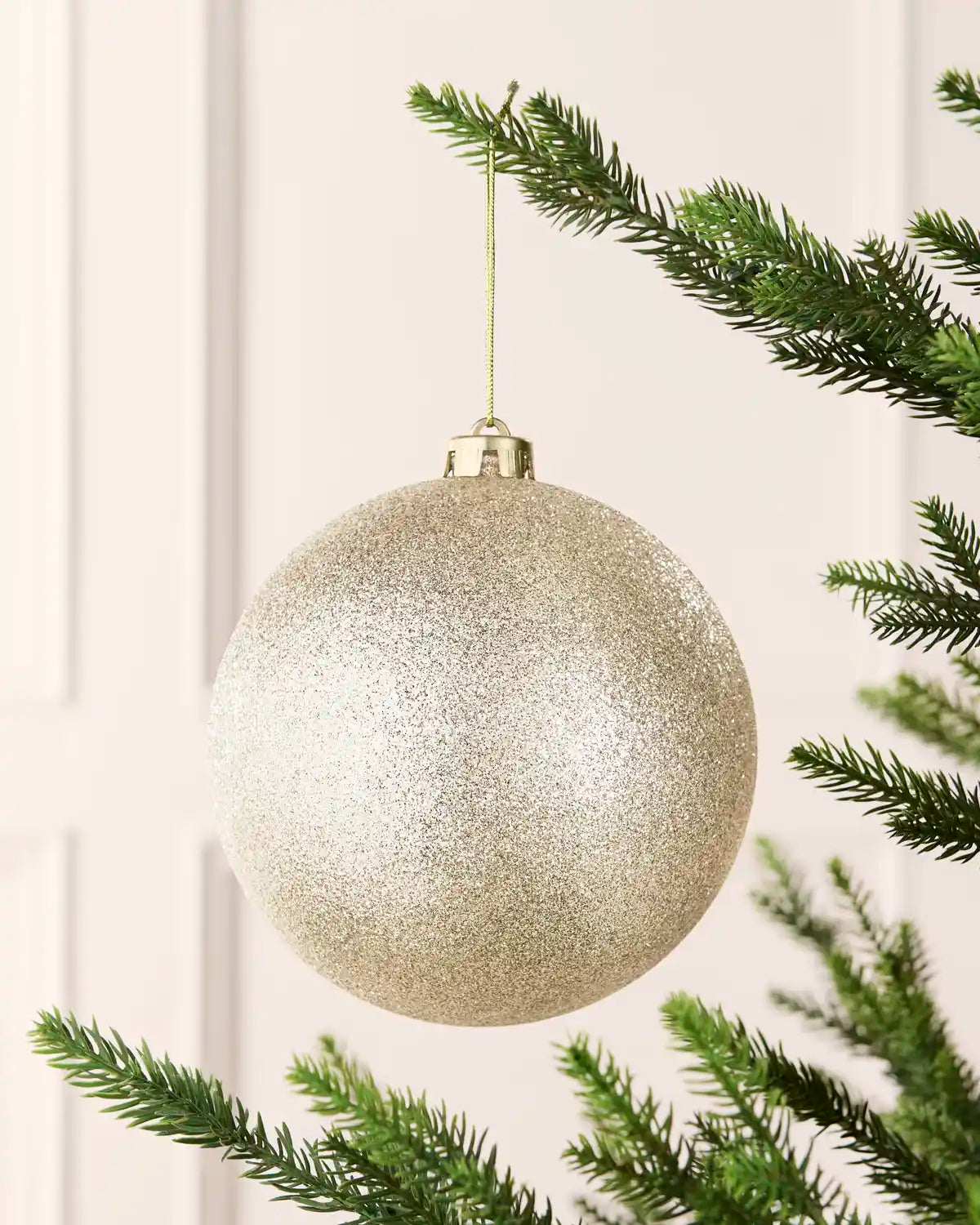 Latte 15 cm oversized glitter shatterproof bauble hanging on a Christmas tree with a gold cap and matching string.
