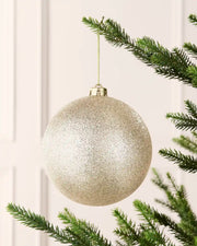 Latte 15 cm oversized glitter shatterproof bauble hanging on a Christmas tree with a gold cap and matching string.
