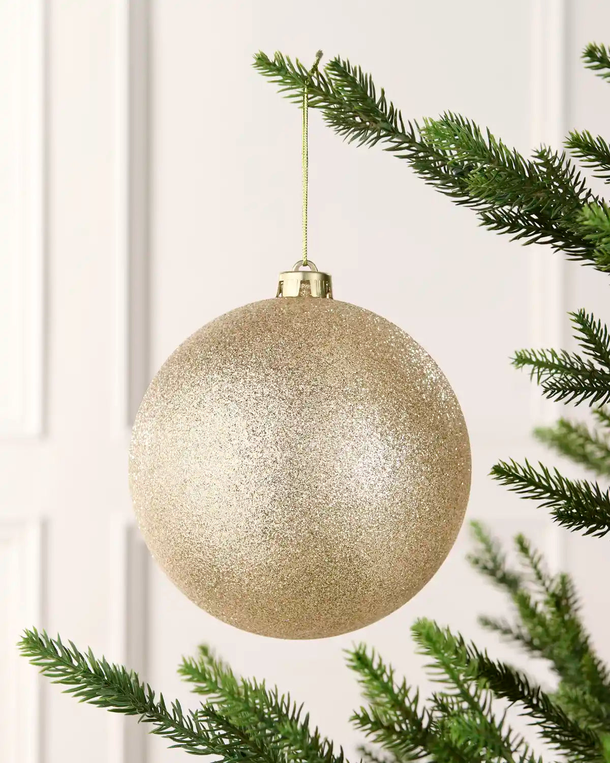 Latte 15 cm oversized glitter shatterproof bauble hanging on a Christmas tree with a gold cap and matching string.
