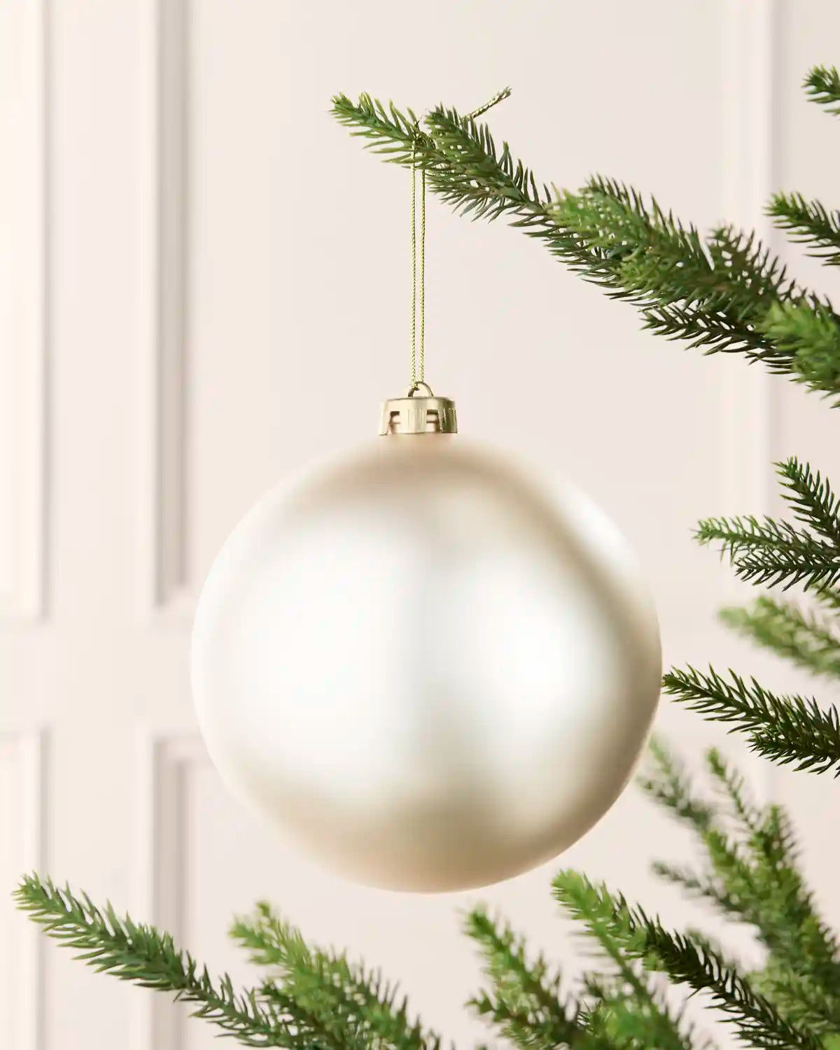 Latte 15 cm oversized matt shatterproof bauble hanging on a Christmas tree with a gold cap and matching string.
