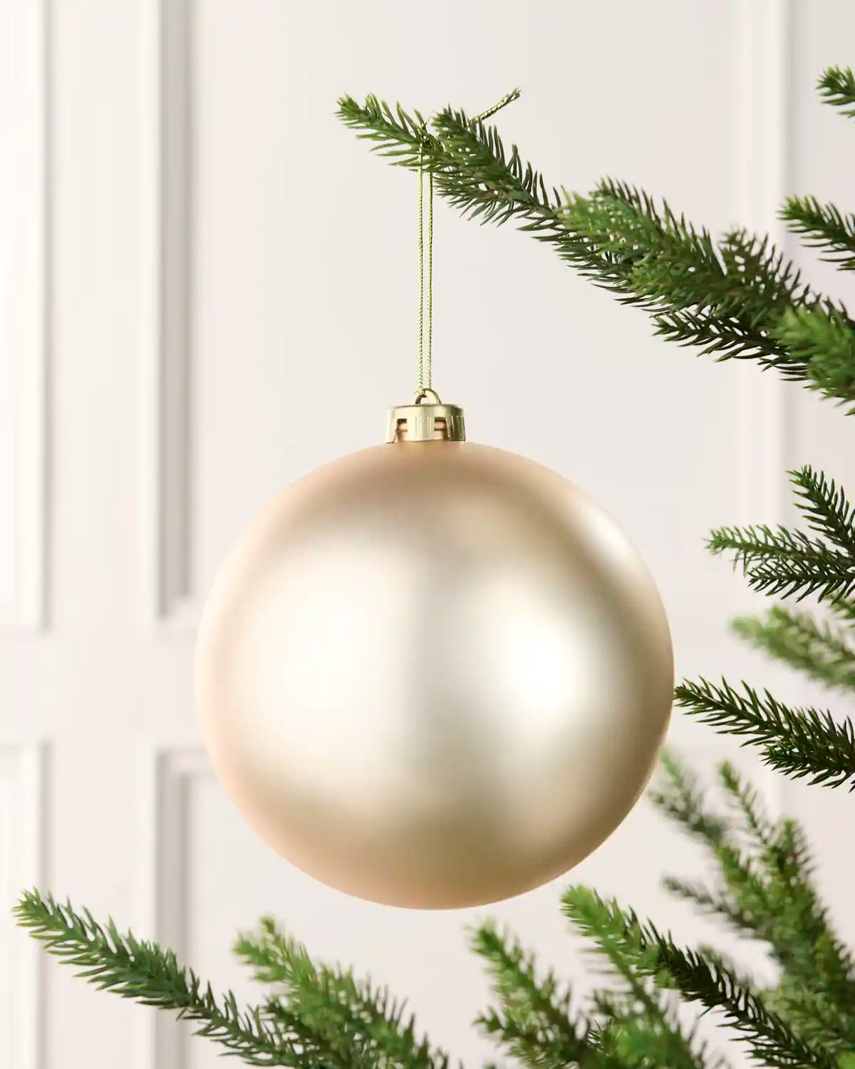 Latte 15 cm oversized matt shatterproof bauble hanging on a Christmas tree with a gold cap and matching string.
