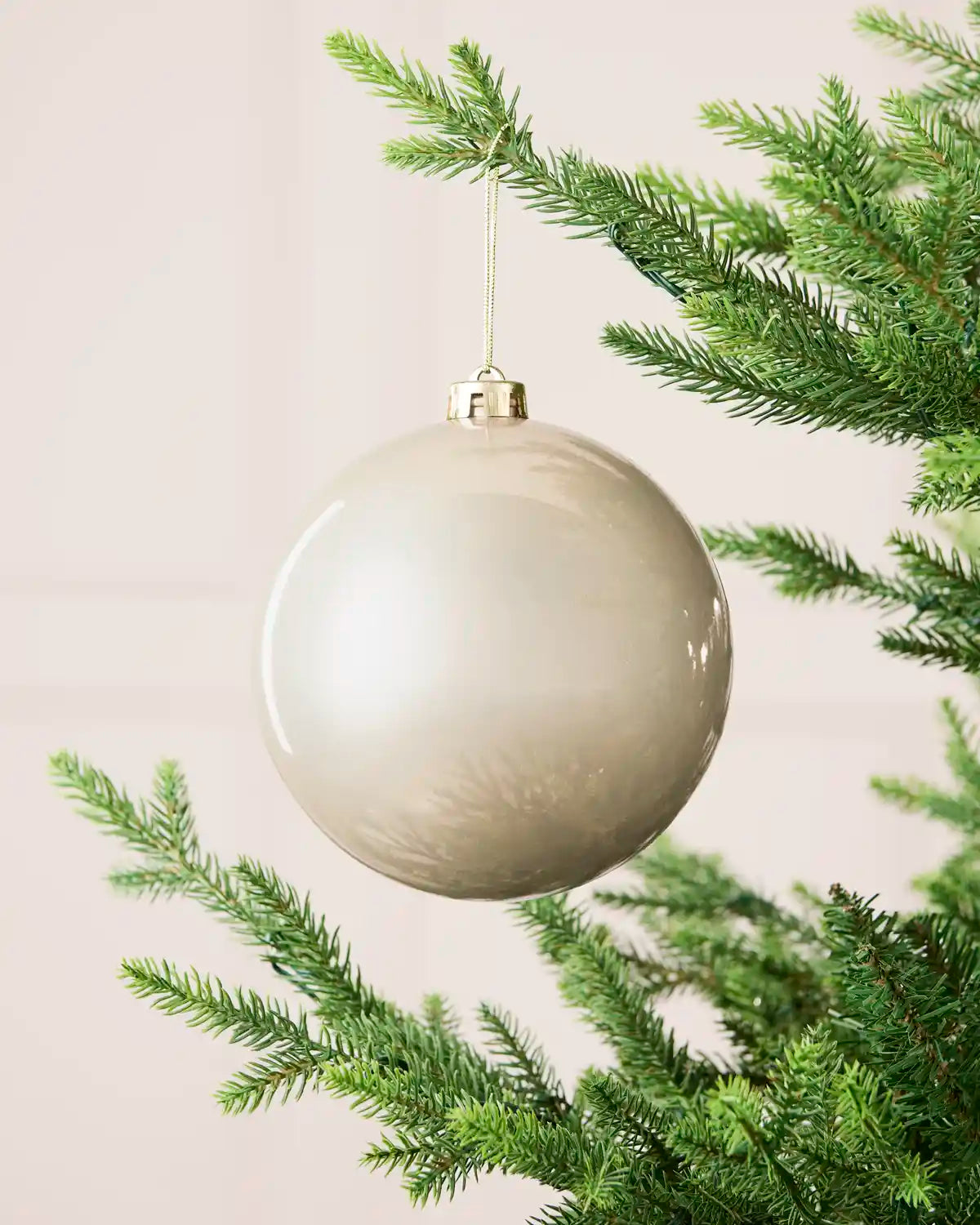 Latte 15 cm oversized shiny shatterproof bauble hanging on a Christmas tree with a gold cap and matching string.
