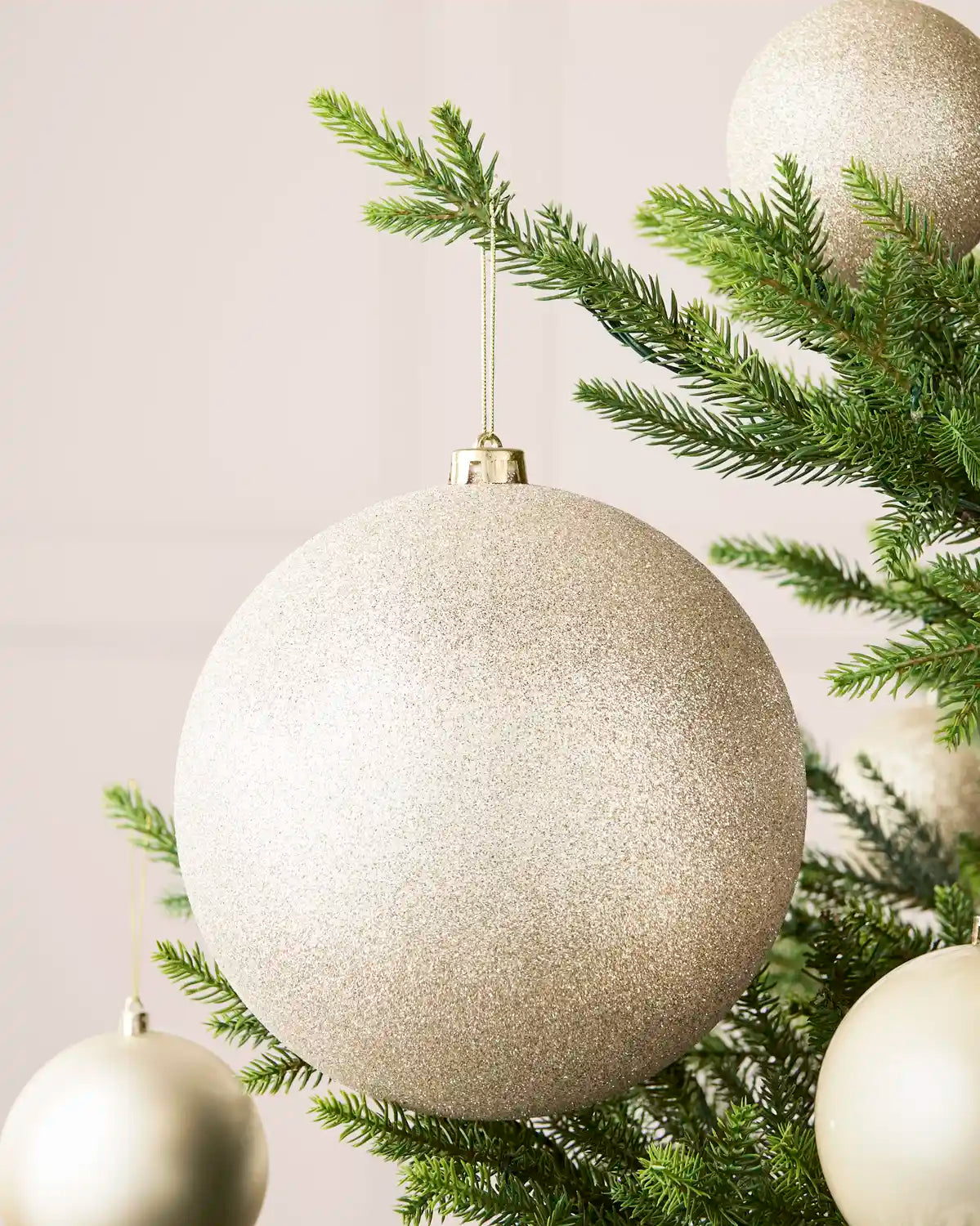 Latte 20 cm oversized glitter shatterproof bauble displayed on a Christmas tree with coordinating latte baubles.
