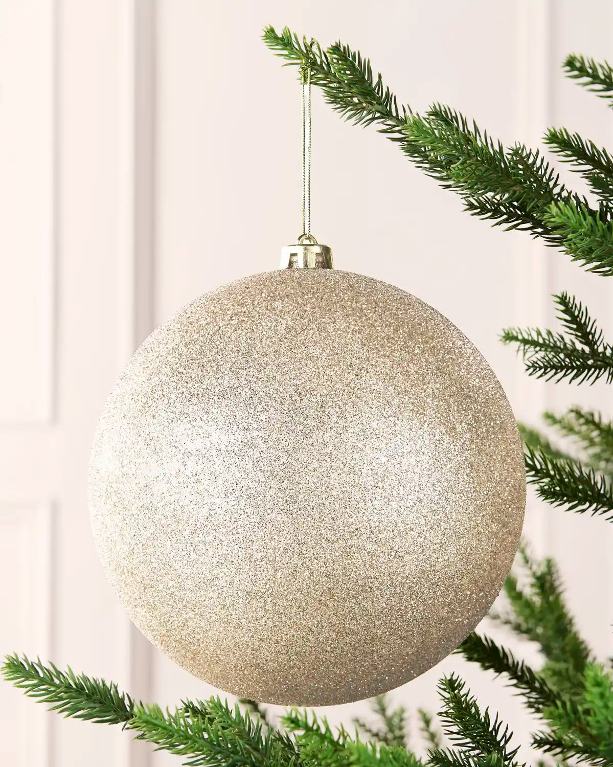 Latte 20 cm oversized glitter shatterproof bauble hanging on a Christmas tree with a gold cap and matching string.
