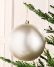 Latte 20 cm oversized matt shatterproof bauble hanging on a Christmas tree with a gold cap and matching string.
