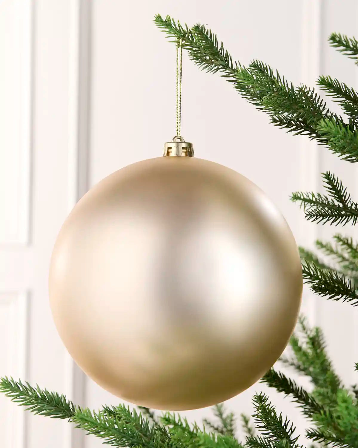 Latte 20 cm oversized matt shatterproof bauble hanging on a Christmas tree with a gold cap and matching string.
