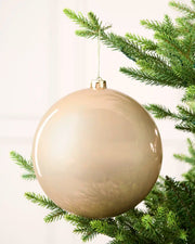 Latte 20 cm oversized shiny shatterproof bauble hanging on a Christmas tree with a gold cap and matching string.
