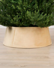 Latte coloured tree skirt holding a green Christmas tree, shown on a light wood floor.
