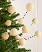 Latte coloured velvet bauble pick on dark brown stems hanging from a Christmas tree against a light background
