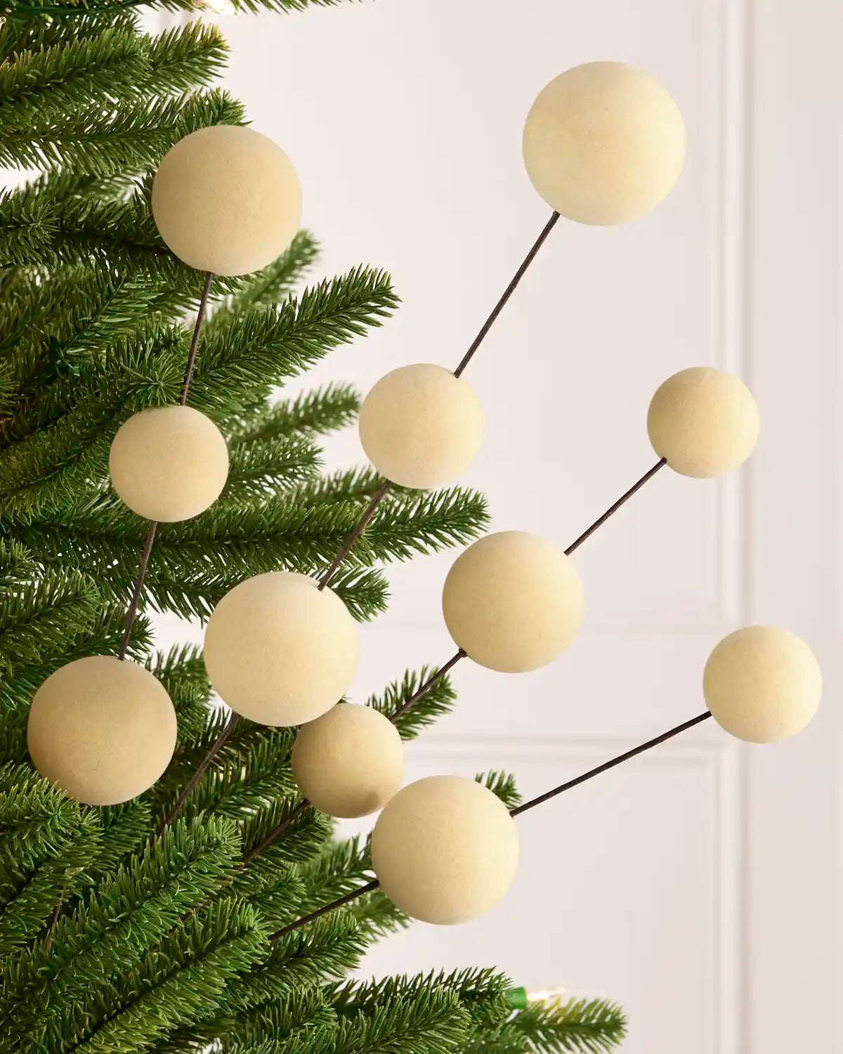 Latte coloured velvet bauble pick on dark brown stems hanging from a Christmas tree against a light background
