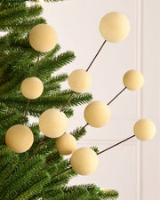 Latte coloured velvet bauble pick on dark brown stems hanging from a Christmas tree against a light background