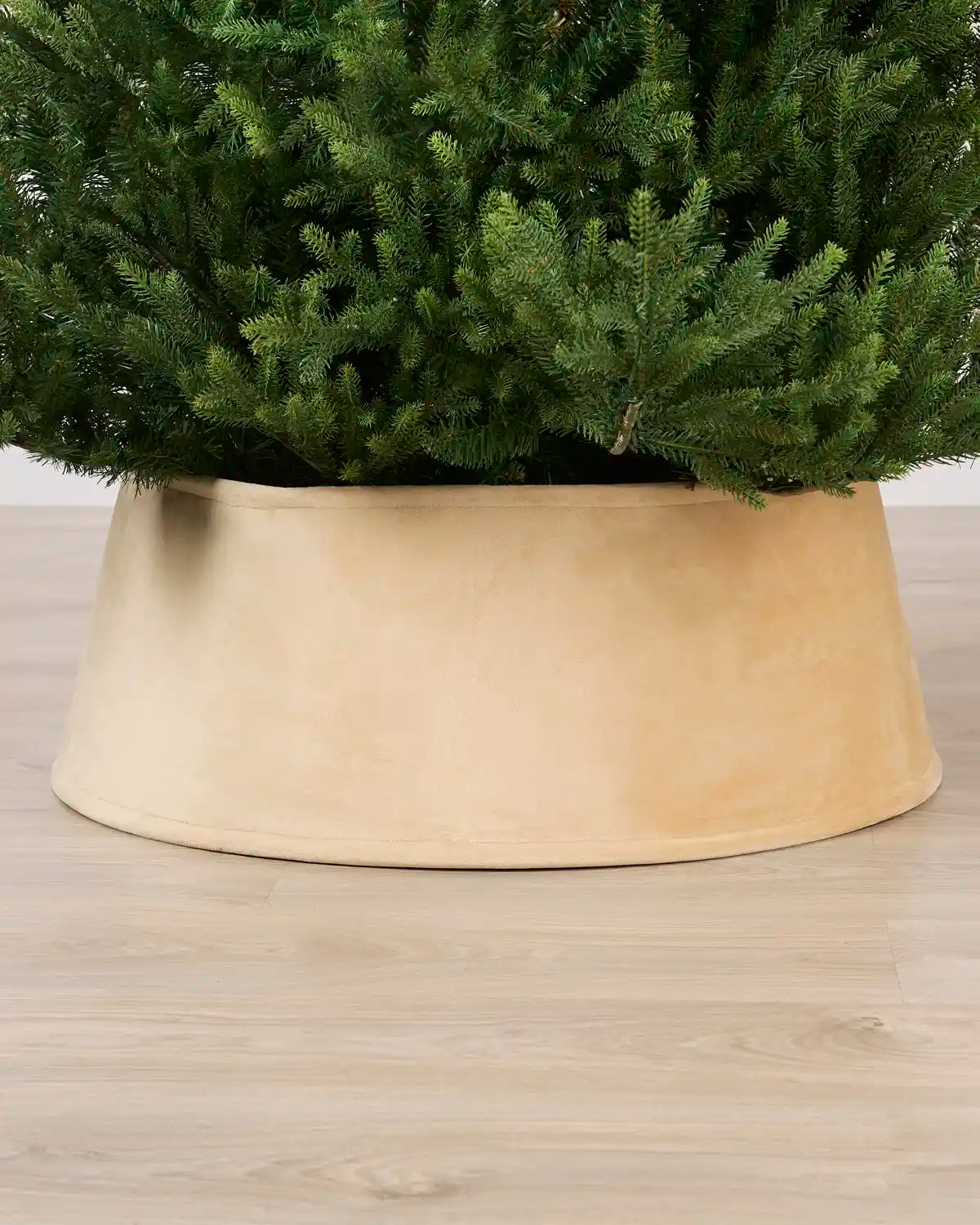 Latte coloured velvet tree skirt under a Christmas tree on a Light brown floor
