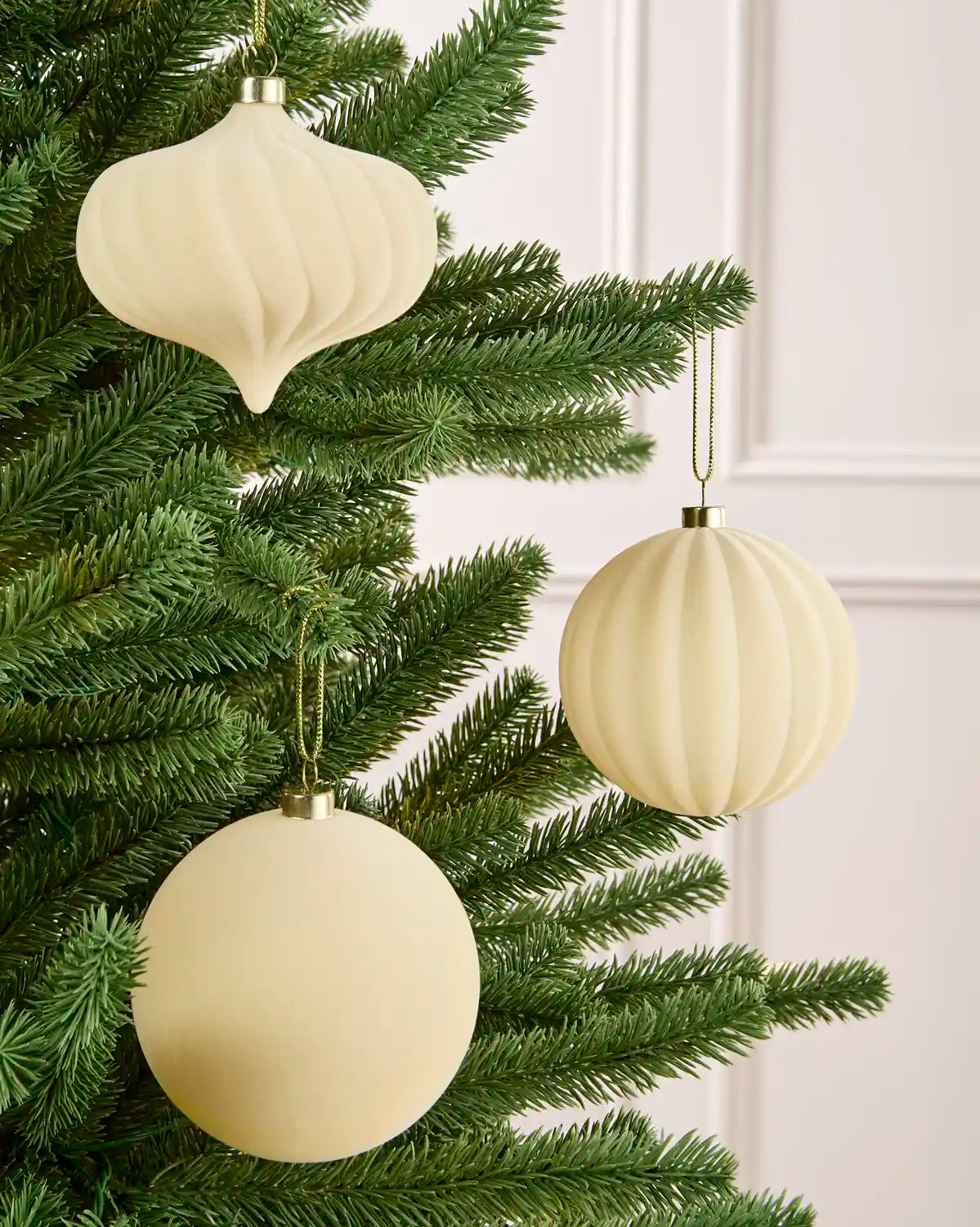 Latte velvet baubles classic round and onion shapes with smooth and swirl patterns, hanging from Christmas tree branches
