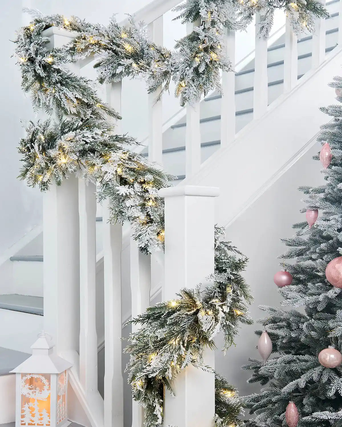 Long view of Pre-Lit Snow-Flocked Fir Garland, 18 ft on White wooden staircase banister with Pink baubles on a Christmas tree