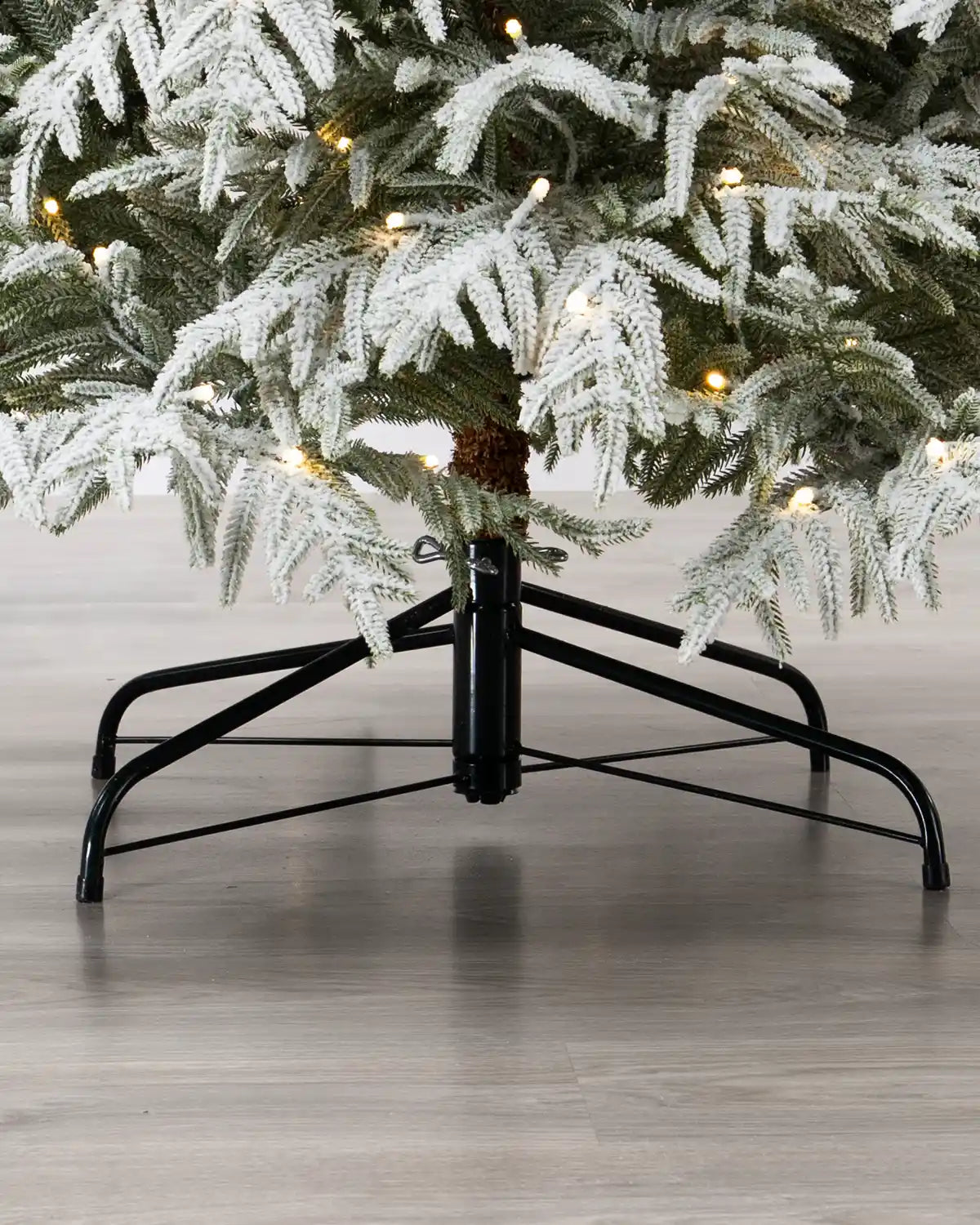 Low-angle view beneath the tree, showing its black metal support stand, central trunk, and illuminated flocked branches