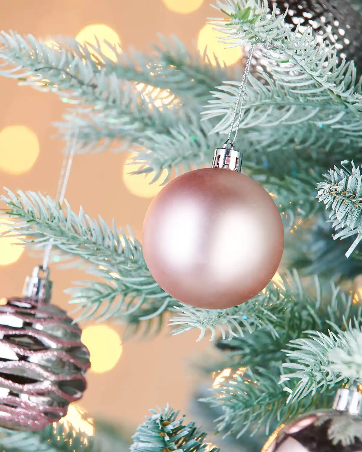 Matt Pink Christmas bauble on a tree with blurred lights in the background