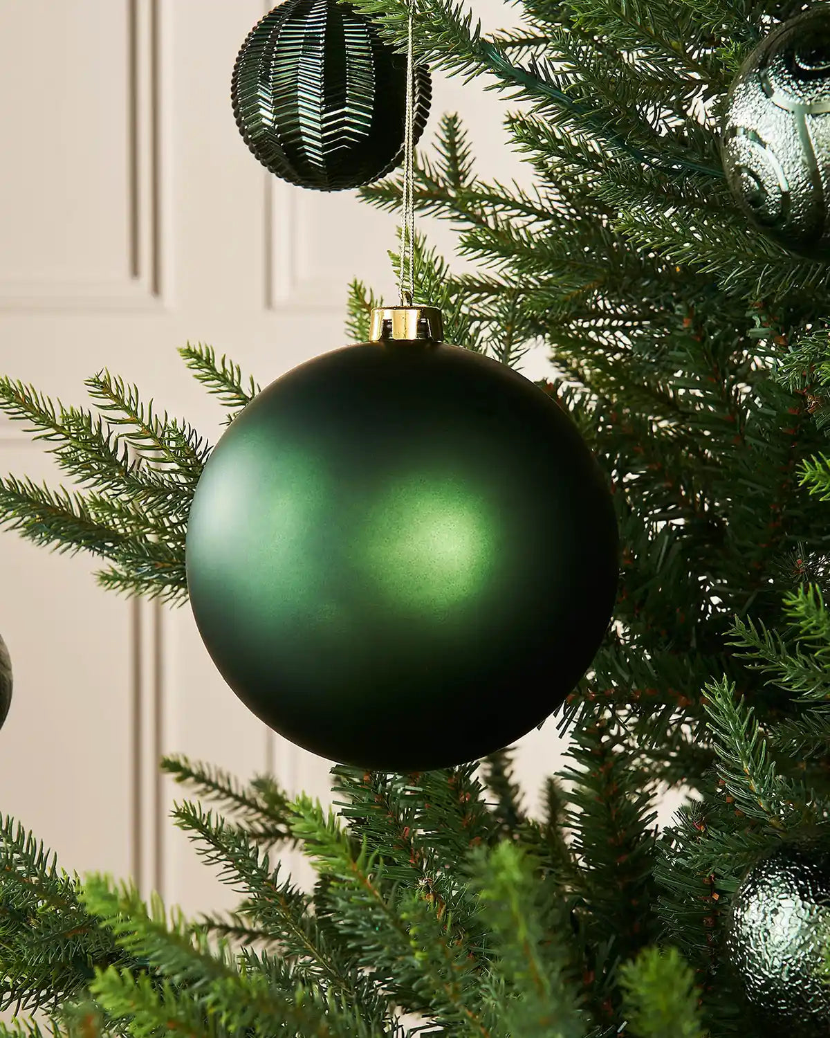 Matt Sage green oversized 15cm Christmas bauble on a Christmas tree branch with 4 smaller sage green baubles in the background