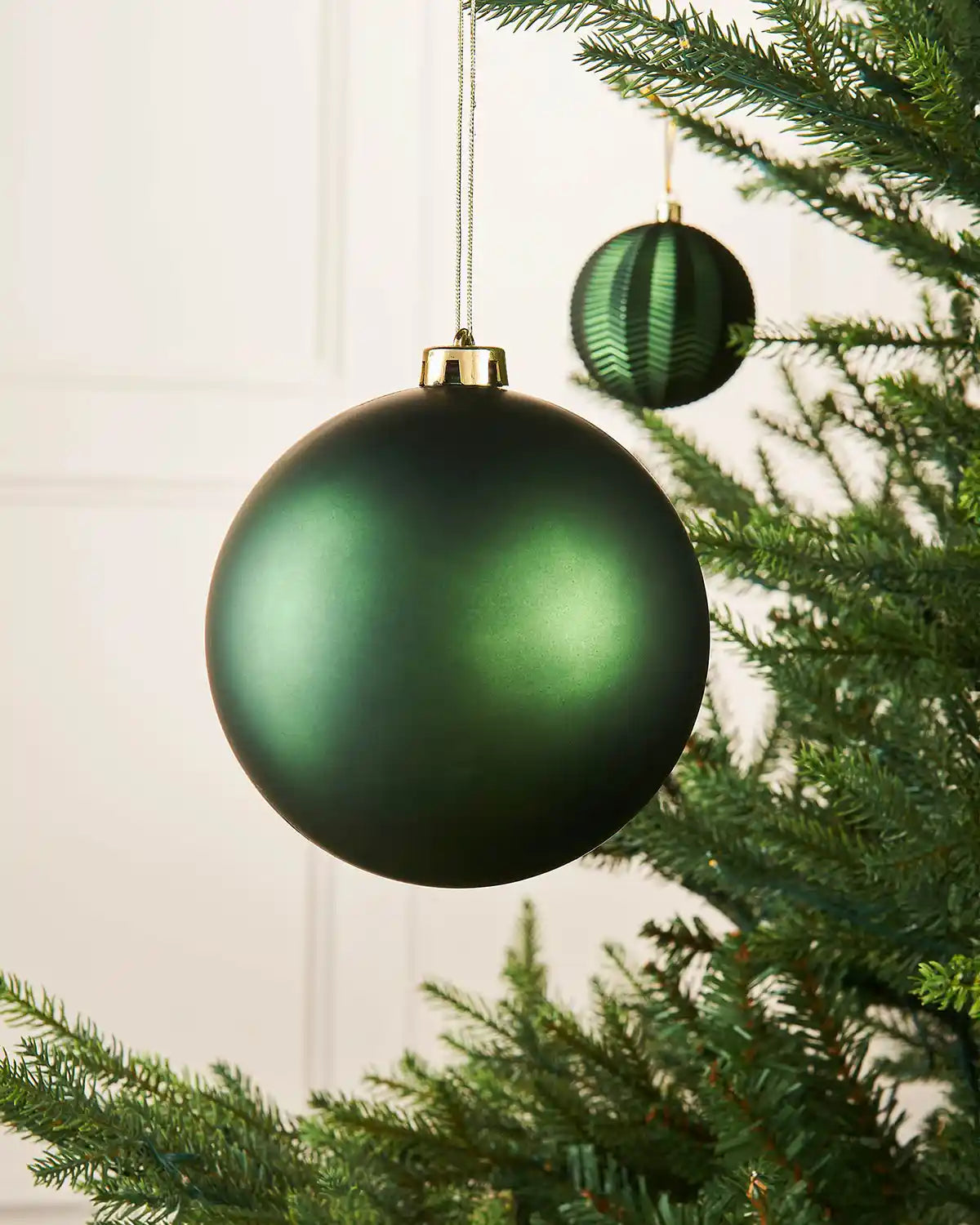 Matt Sage green oversized 15cm Christmas bauble on a Christmas tree branch with a smaller sage green bauble in the background