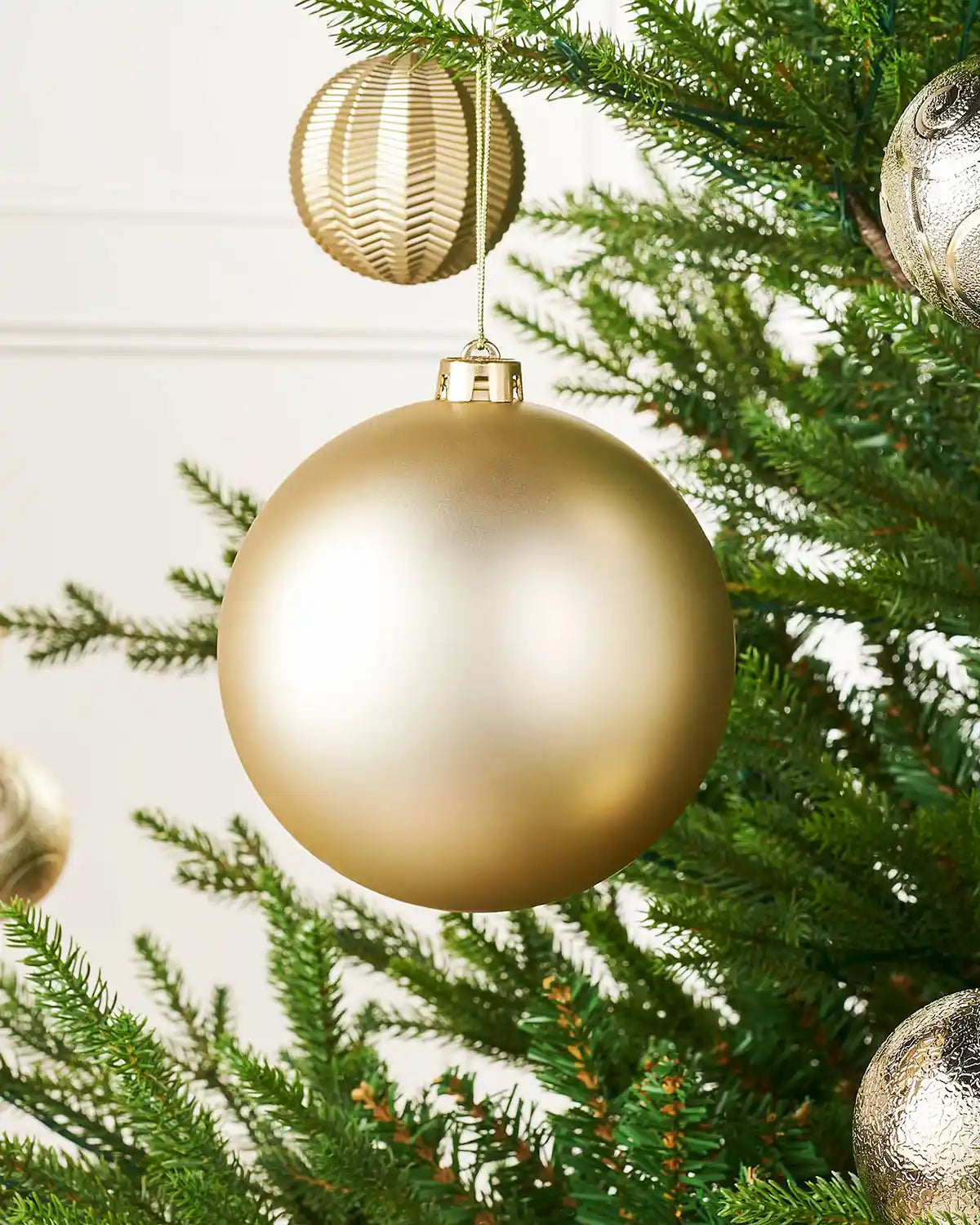 Matt gold 15cm oversized bauble on a Christmas tree branch with 4 smaller gold baubles in background
