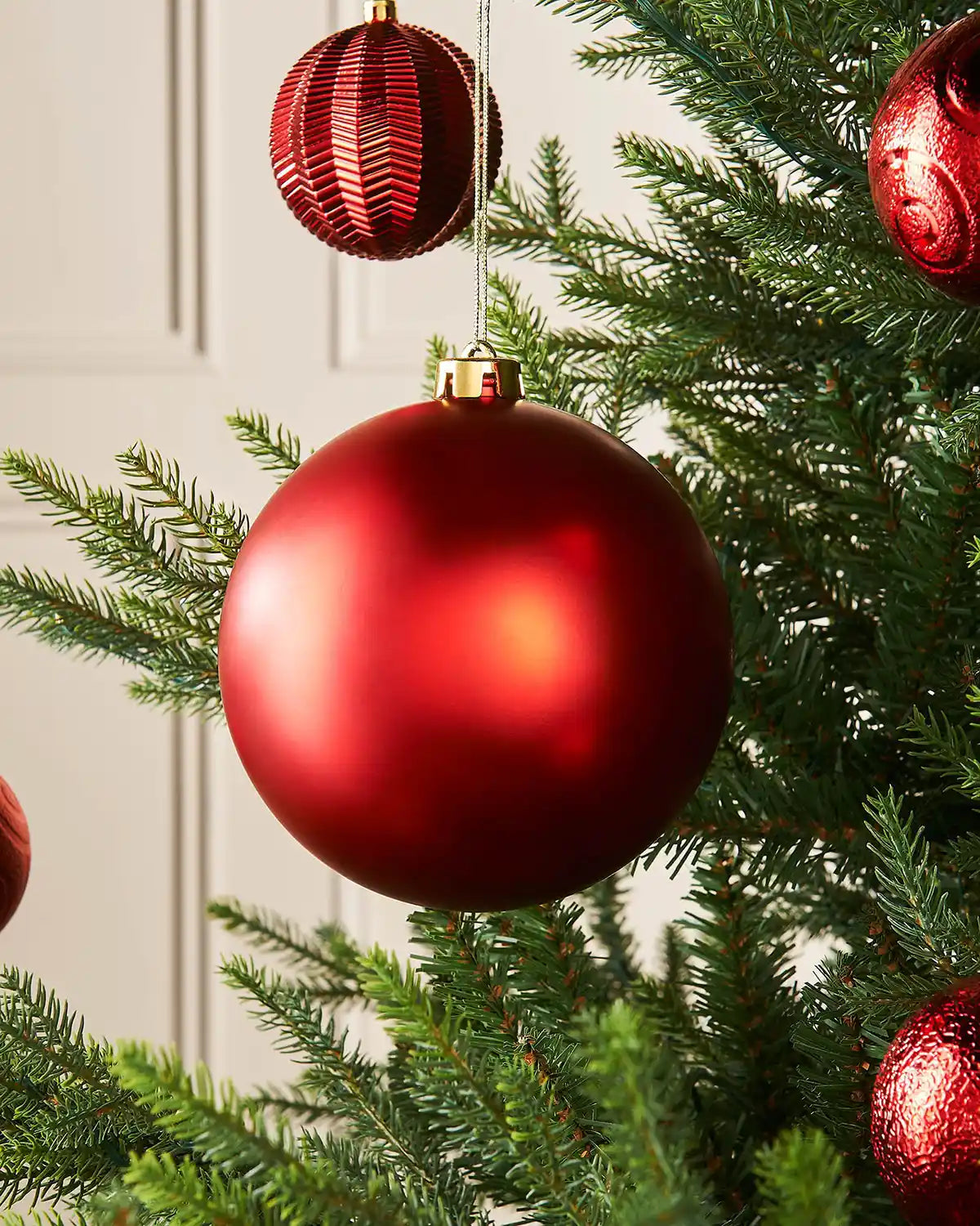 Matt red 15cm oversized bauble on a Christmas tree branch with 4 smaller red baubles in the background 