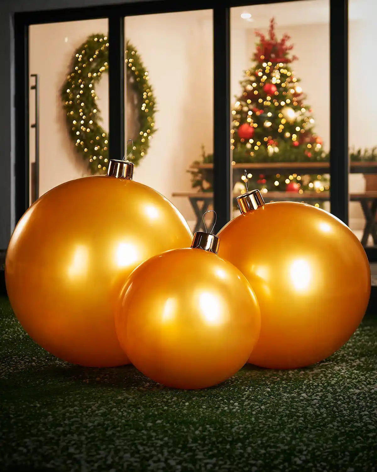 Medium, large and extra large gold Christmas inflatable baubles  on a grassy surface with a festive background.