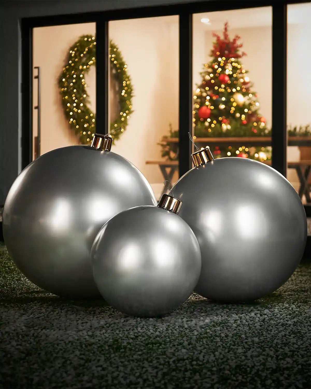 Medium, large and extra large silver Christmas ornaments on a grassy surface with a festive indoor background.