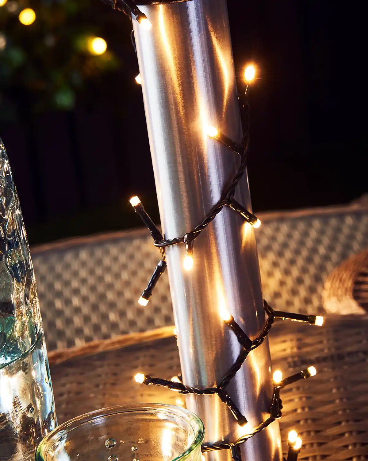 Metallic cylindrical object with string lights wrapped around it, on a blurred background