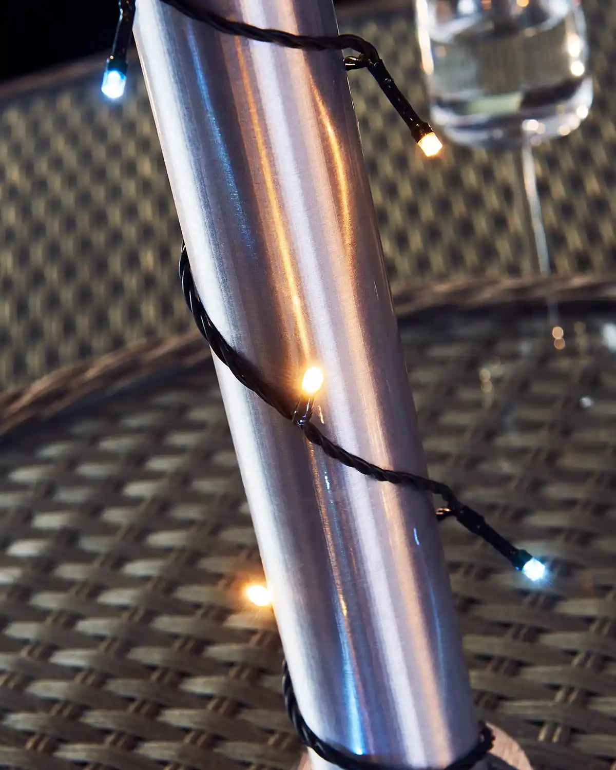 Metallic cylindrical pole with warm white and ice white string lights on a textured surface