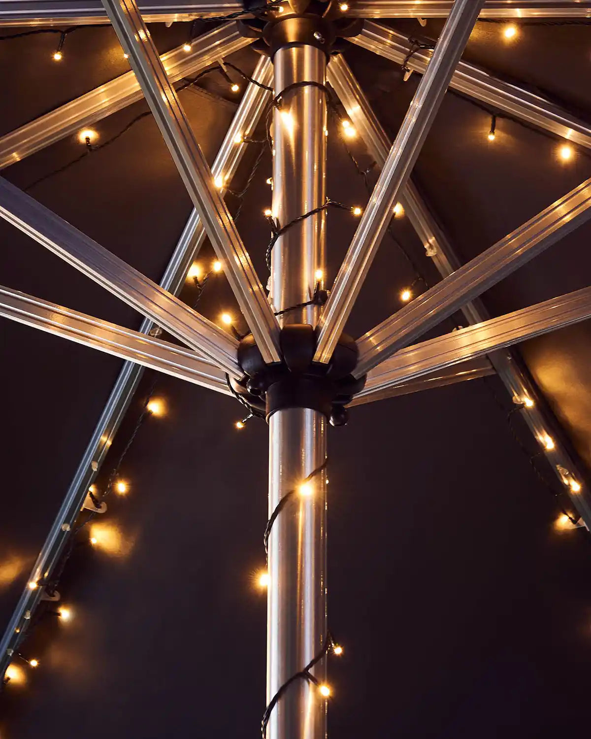 Metallic outdoor umbrella with warm white string lights against a dark background