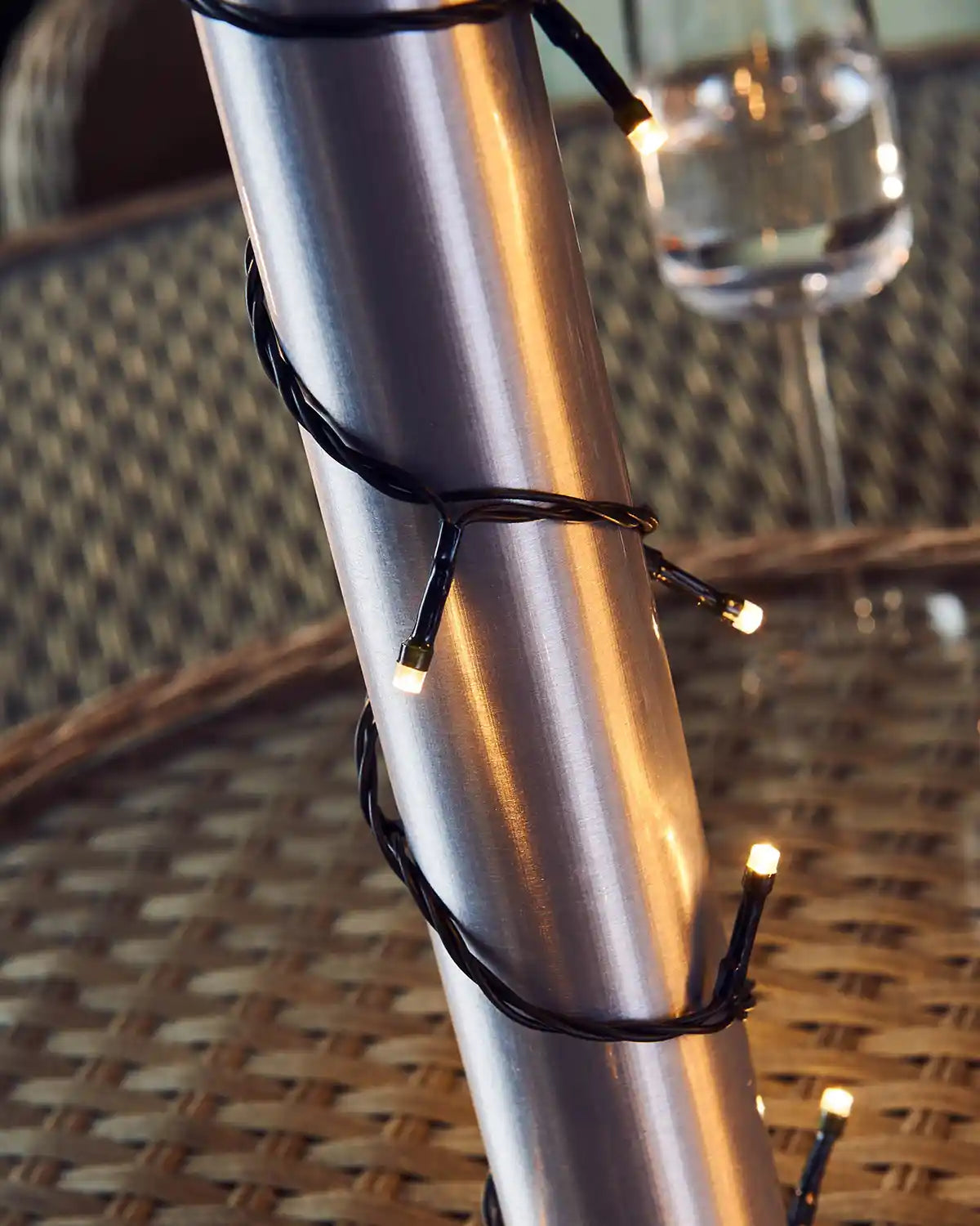 Metallic pole with warm white string lights on a wicker chair and table