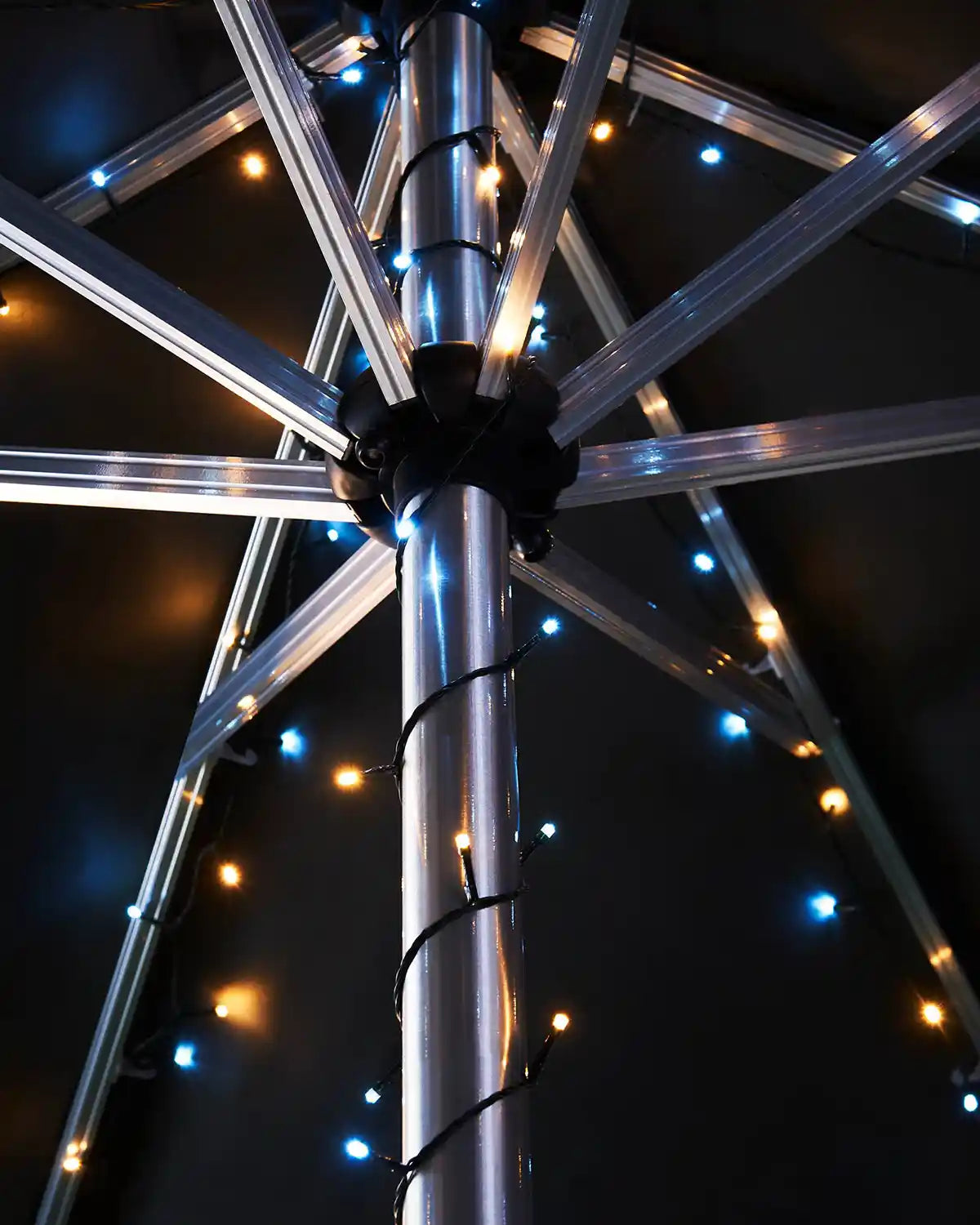 Metallic umbrella pole with warm white and icy white string lights against a dark background