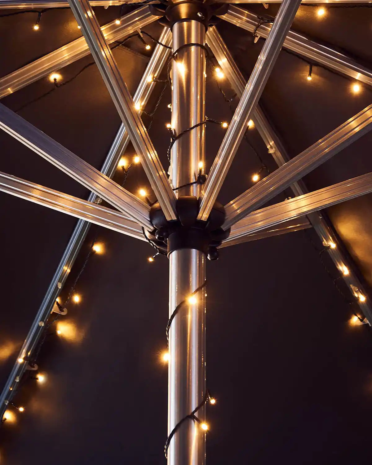 Metallic umbrella pole with warm white string lights against a dark background