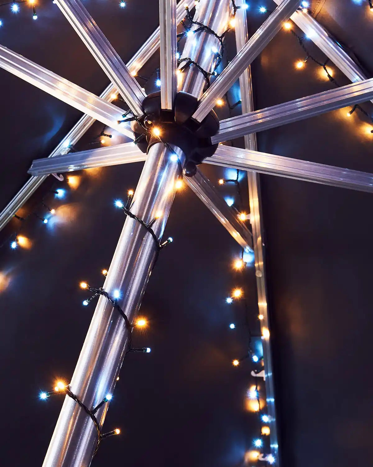 Metallic umbrella with warn white and ice white string lights against a dark background