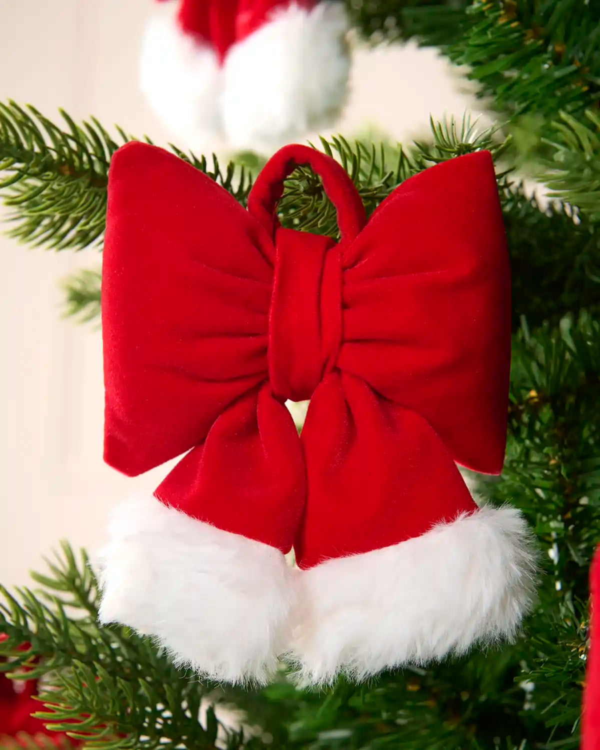 Mini Hat style bows on a Christmas tree with blurry bows in the background against a cream wall