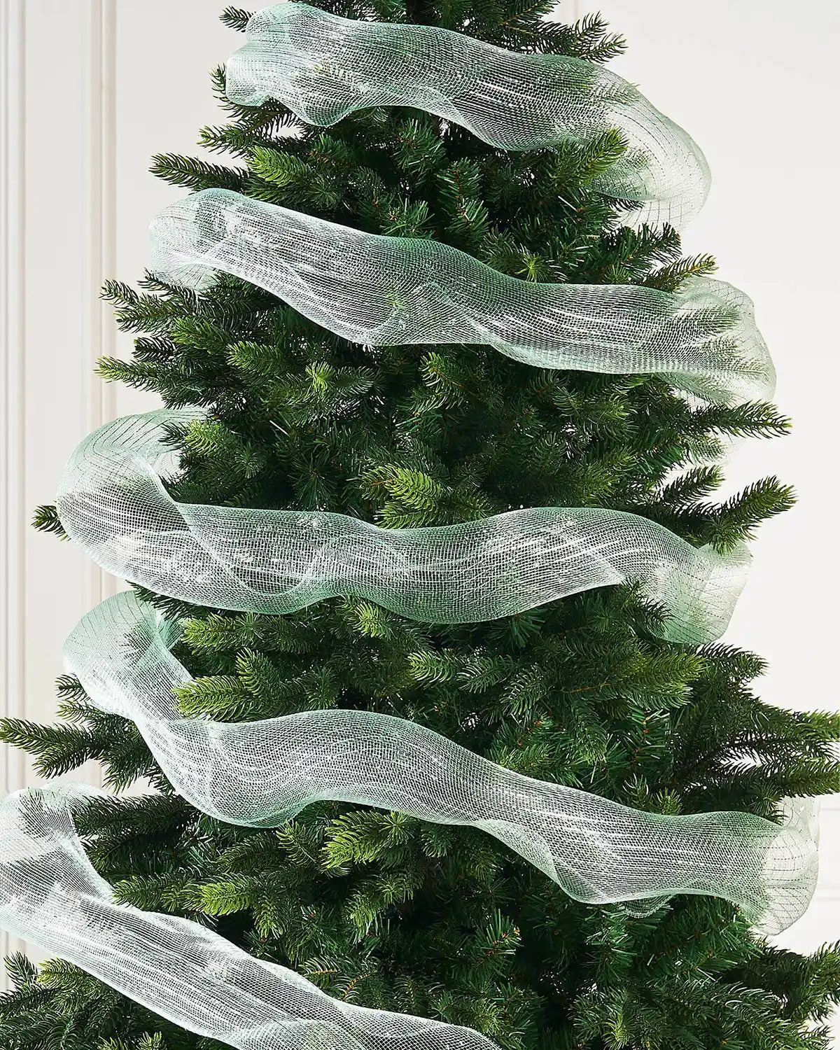 Mint green mesh fabric ribbon wrapped around Christmas tree against a cream panel wall
