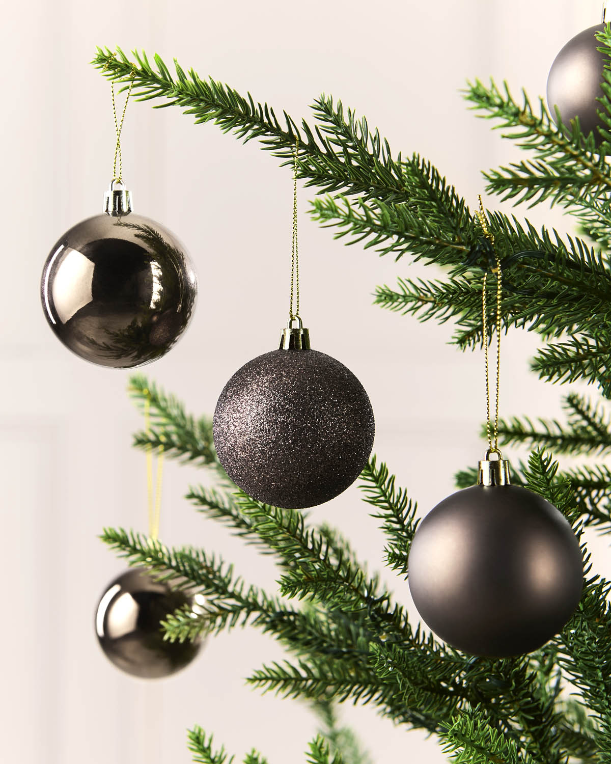 Mocha Christmas tree ornaments in three finishes—shiny chrome, glittery, and matte—hanging from the green branches of a Christmas tree against a soft, light beige background.