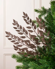 Mocha Leaf Christmas Tree Spray placed in Christmas tree branches with plain cream background. 