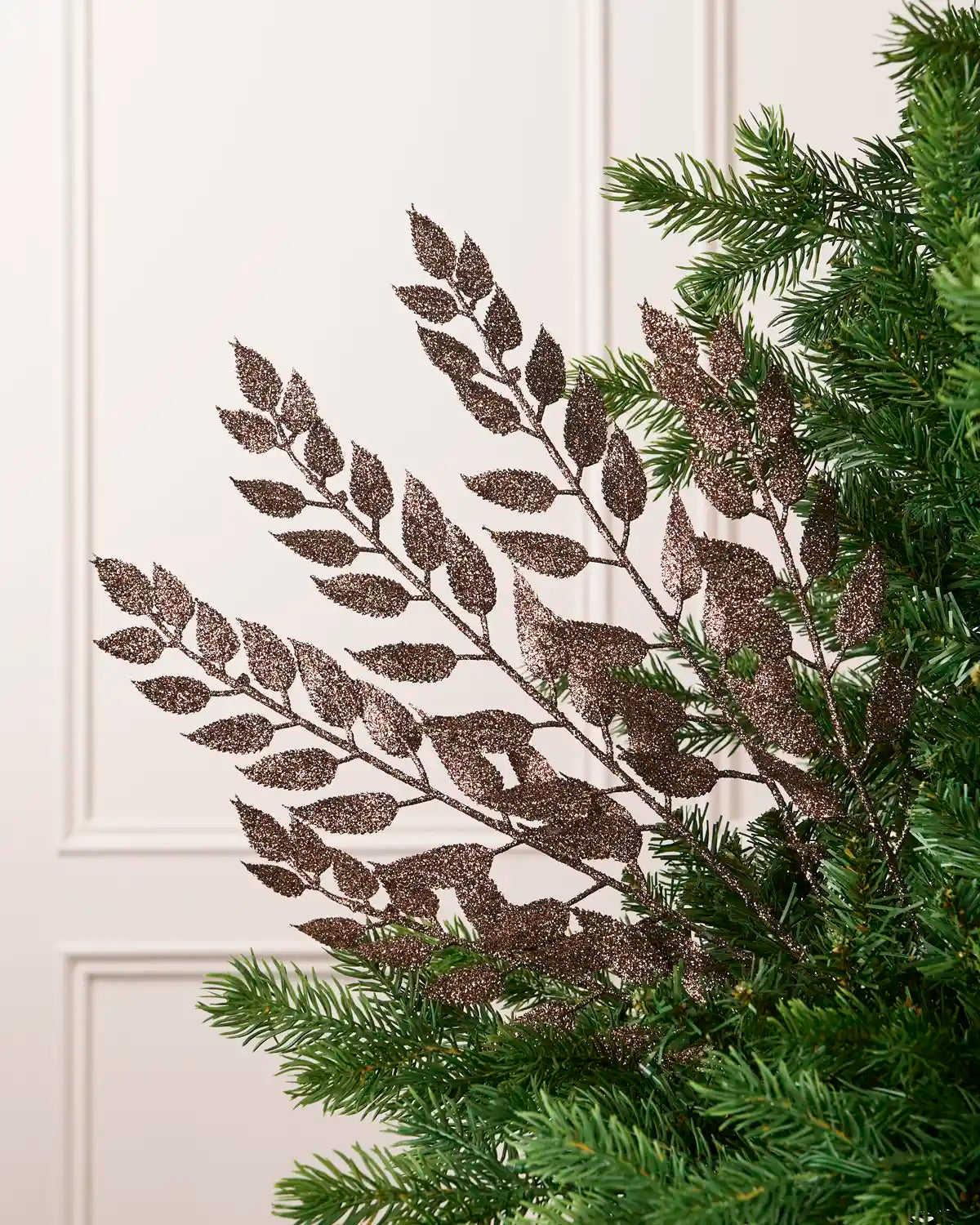 Mocha Leaf Christmas Tree Spray placed in Christmas tree branches with plain cream background. 