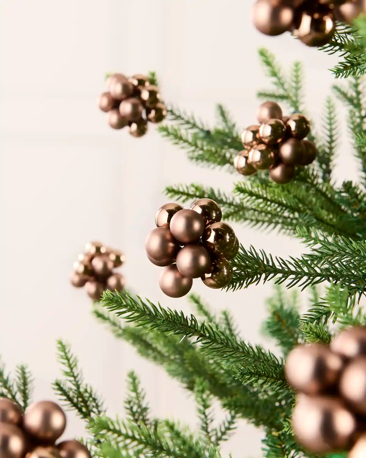 Mocha cluster baubles on a Christmas tree branch with other cluster baubles blurry in the background against a cream wall